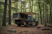 Pickup truck bed tent with expandable awning set up at forest campsite