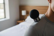 Percussion massage gun close-up in use on upper back and shoulder