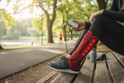 Person wearing red light ankle therapy wrap outdoors with power bank